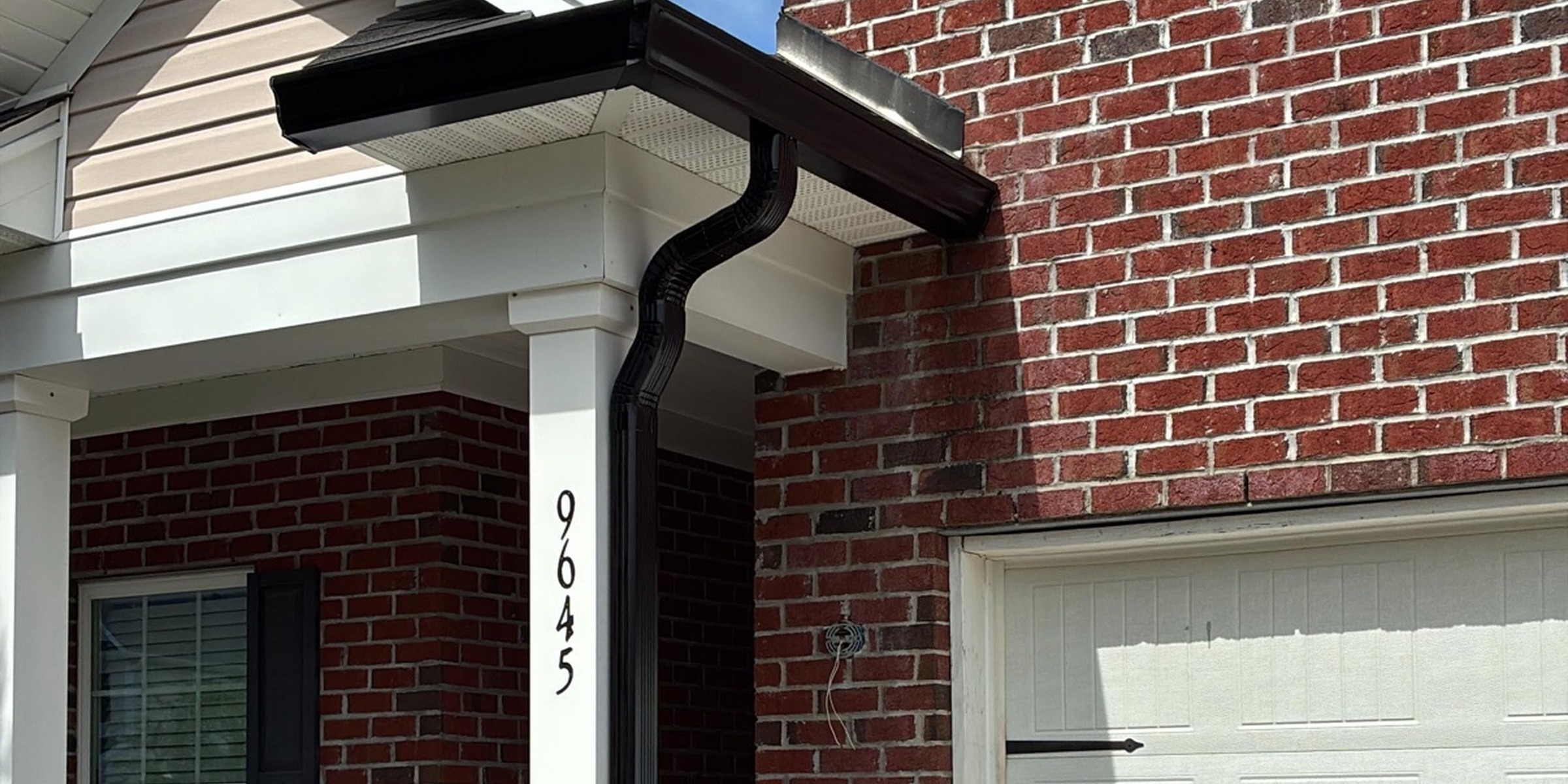 Black gutter and downspout fitted to the corner of a brick home.