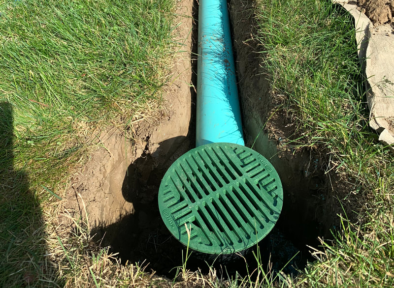 Underground downspout drain installation with green drainage grate in yard